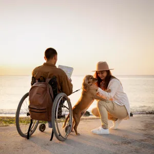 A man in a wheel chair with her girlfriend and pet at the beach